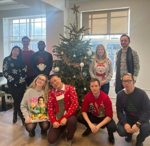 Alliotts staff in Christmas jumpers, standing by a Christmas tree