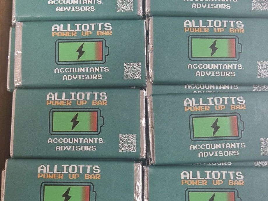 Showing lots of chocolate bars. They have custom wrappers saying 'Alliotts Power Up Bar' and show a charging symbol and a QR that links to the video games page on the Alliotts website